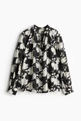 Blusa oversized con cuello elevado fruncido, abertura en V adelante y bajo recto. Mangas globo largas de corte raglán con abertura y botón en los puños.