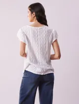 Blusa blanca labrada con cuello a la base, escote en V y aplique metálico. Tiene mangas cortas superpuestas.