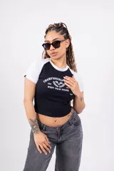 Remera corta blanca con mangas raglán negras, cuello redondo y estampado frontal con el texto "Championship League Est. 1996 West Palm Beach" y dos raquetas de tenis cruzadas.