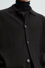 Cárdigan negro de punto con cuello solapa, manga larga y cierre frontal con botones.