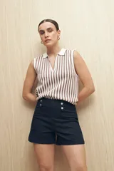 Short de jean negro de tiro alto con detalle de doble botón metálico en la cintura, bolsillos delanteros y traseros.