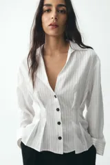 Camisa blanca con rayas verticales finas en color gris, de corte entallado, con cuello solapa y escote en pico. Cierre frontal con botones negros.