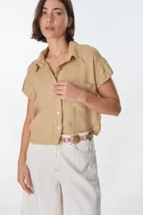 Camisa color beige de lino, con cuello clásico, manga corta con detalle de frunce y bolsillo de parche en el pecho.