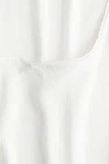 Musculosa blanca de punto pointelle suave, corte ajustado, con escote cuadrado, moño de satén y bajo sobrehilado.
