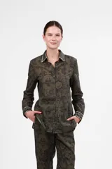 Camisa verde militar con estampado de soles, animales y motivos arquitectónicos en negro. Tiene cuello clásico y puños con ribete blanco.