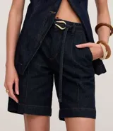 Bermuda de jeans azul oscuro, tiro medio, con costuras contrastantes y cinturón de lazo de tela con hebilla metálica de forma irregular.