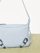 Mini cartera bandolera color celeste con textura granulada, correa fina al tono y detalles de hebillas metálicas plateadas.