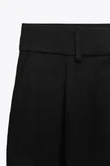 Pantalón negro de tiro alto con bolsillos delanteros, pinzas y corte ancho.
