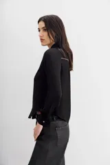 Camisa negra de manga larga, estilo texana, con cuello camisero y botones metálicos tipo snap. Presenta un bordado de tachas termo fijadas en forma de pico en la zona del pecho y hombros.