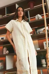 Vestido largo de lino en color celeste, con cuello camisero, manga corta y cierre frontal con botones. Presenta bordados decorativos en contraste en la pechera y en el ruedo.