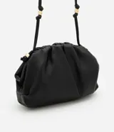 Cartera transversal pequeña de cuero sintético color negro, con asa de cordón y detalles metálicos dorados.