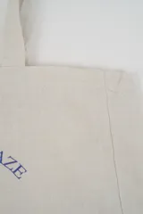 Bolso tote de tela con estampado de rayas verticales rosadas y blancas, laterales y asas en color beige. Presenta la palabra "BONJOUR" en verde en el centro y "INDIAN" en la parte inferior.