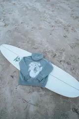 Buzo canguro gris con capucha y cordones ajustables. Estampado en la espalda con una sirena, una flor de hibisco y la frase "Glass Waves".