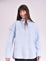 Camisa celeste de corte amplio, con cuello clásico, cierre frontal con botones, bolsillo en el pecho y mangas largas con detalle de botones en los puños.