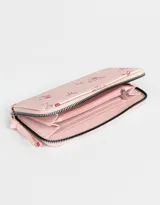 Billetera de cuerina color crema con estampado de flores y moños. Tiene formato rectangular, cierre circundante con tirador y múltiples compartimentos internos.