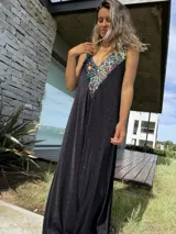 Vestido largo negro con escote en V y breteles finos. Presenta un aplique de lentejuelas multicolores en el escote.