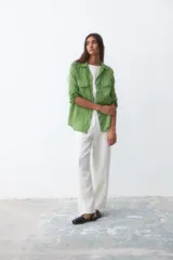 Camisa verde de lino con cuello clásico, cierre frontal con botones, mangas largas con trabilla para enrollar y dos bolsillos con solapa en el pecho.