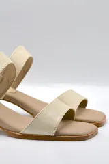 Sandalias de cuero color beige con taco cuadrado y tira ancha sobre los dedos. Presenta pulsera al tobillo con hebilla dorada.