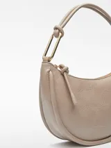 Bolso de hombro tipo media luna color beige, con textura craquelada, cierre de cremallera y asa tubular con pieza metálica.