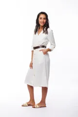 Vestido camisero blanco de poliéster con corte midi, cuello camisero, mangas largas con puños abotonados, cierre frontal con botones y cinturón marrón.