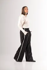 Pantalón negro de tela deportiva con cintura elástica ancha y cordón ajustable. Presenta corte amplio, bolsillos laterales y una franja blanca vertical a lo largo de cada pierna.