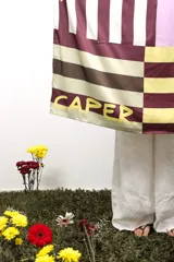 Pañuelo rectangular con diseño de bloques de color en tonos borgoña, amarillo, marrón y lila. Incluye la palabra 'CAPER' estampada en amarillo. 