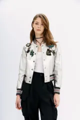 Campera bomber de cuero ovino color plateado, con cuello, puños y ruedo de ribb metalizado. Presenta apliques de parches bordados con lentejuelas y mostacillas.