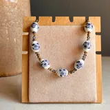 Collar con cuentas de cerámica blanca con diseño floral azul y cuentas de cristal facetado color dorado y gris.