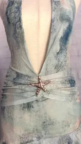 Minivestido con estampado abstracto en tonos celeste, verde y blanco. Escote halter con lazos en la nuca, espalda descubierta y falda con volados.