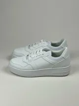 Calzado deportivo simil cuero en tonos blanco y beige, con detalles de perforaciones y suela de goma.