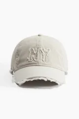 Gorra de béisbol color beige con aplique bordado de las letras "NY" en el frente y visera con efecto desflecado.