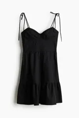 Vestido corto negro de popelina de algodón con breteles finos ajustables con moña, escote corazón y cuerpo entallado con costuras decorativas y espalda fruncida. Falda acampanada con costura fruncida en el bajo.