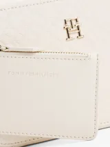 Bandolera Tommy Hilfiger color crema con monograma TH en relieve. Tiene correa ancha ajustable y extraíble, cierre de cremallera, bolsillo interior con cremallera y monedero extraíble con cremallera.