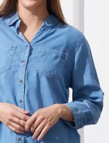Camisa celeste de tencel con cuello con solapa, escote en V, abertura central con botones, bolsillo aplicado en el frente y ruedo desflecado.