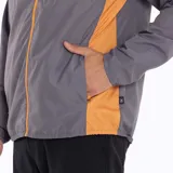 Cortaviento gris con detalles en naranja, ultra liviano, de secado rápido, con capucha y bolsillos internos.