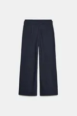 Pantalón negro con finas rayas verticales blancas, de tiro medio y corte ancho. Presenta bolsillos delanteros y traseros, cintura doble tipo bóxer con botones y cierre frontal con cremallera y ganchos metálicos. Detalle de franja marrón en los laterales.