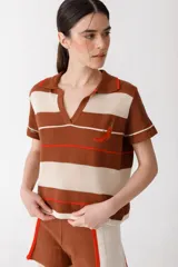 Remera polo tejida a rayas horizontales rojas y rosadas, con cuello clásico y bordado de ají verde.