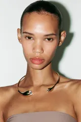 Vestido midi marrón de tejido de punto con escote recto y hombros descubiertos. Presenta detalle de collar metálico con aplicación de joyas, forro interior, bajo con abertura en la espalda, frunces en el tejido y cierre con cremallera oculta en la costura.