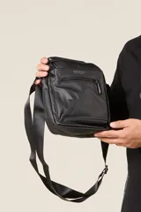 Bandolera negra con correa ajustable y cierre superior.