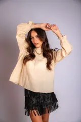 Camisa color crema con cuello alto y mangas largas con volados en los puños. Presenta detalles de crochet y broderie en el frente.