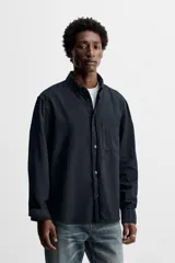 Camisa azul de algodón con textura chambray, corte regular fit, cuello abotonado, manga larga con puños abotonados, bolsillo de parche en el pecho y cierre frontal con botones.