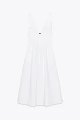 Vestido midi blanco de algodón, con escote pico pronunciado y tirantes anchos ajustables con lazada. Presenta elástico en la cintura y falda con pliegues.