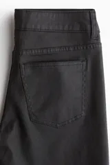 Jean de cinco bolsillos color negro, con tiro bajo y cierre de botón. Presenta un corte ajustado en la parte superior y piernas acampanadas.