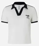 Blusa polo de malla de algodón color blanco con cuello y mangas cortas con ribete negro. Presenta bordado de moña en el pecho y dos rayas negras en cada manga.