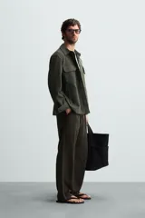 Sobrecamisa color beige de corte relaxed fit, confeccionada en tejido con elasticidad. Tiene cuello solapa, manga larga con puños abotonados, bolsillos de parche con solapa en el pecho y bolsillos de ojal en la cadera. El cierre es frontal con botones.