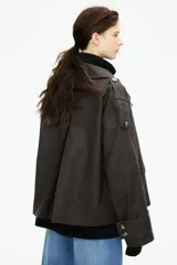 Gabardina corta color marrón chocolate, de corte holgado, con cuello clásico, doble botonadura, charreteras, trabillas abotonadas en los puños, bolsillos delanteros con solapa y pliegue invertido en la espalda. Forrada.