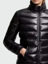 Campera puffer corta de nylon laqué color negro, con relleno de plumas, capucha desmontable, cierre frontal con cremallera y bolsillos laterales con cremallera.