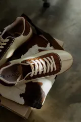 Zapatillas bajas color crema con detalles en marrón y cordones blancos.