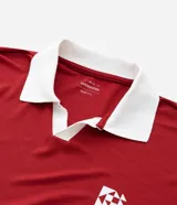 Remera de manga corta estilo polo, color rojo, con cuello y puños en contraste blanco. Presenta un corte oversized con hombros caídos y la palabra "ATHLÈTES" estampada en blanco en el frente. Incluye pequeños gráficos blancos a cada lado del pecho.