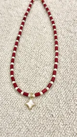 Collar corto con cuentas cilíndricas rojas y blancas alternadas, y dije colgante en forma de estrella de nácar con borde dorado.